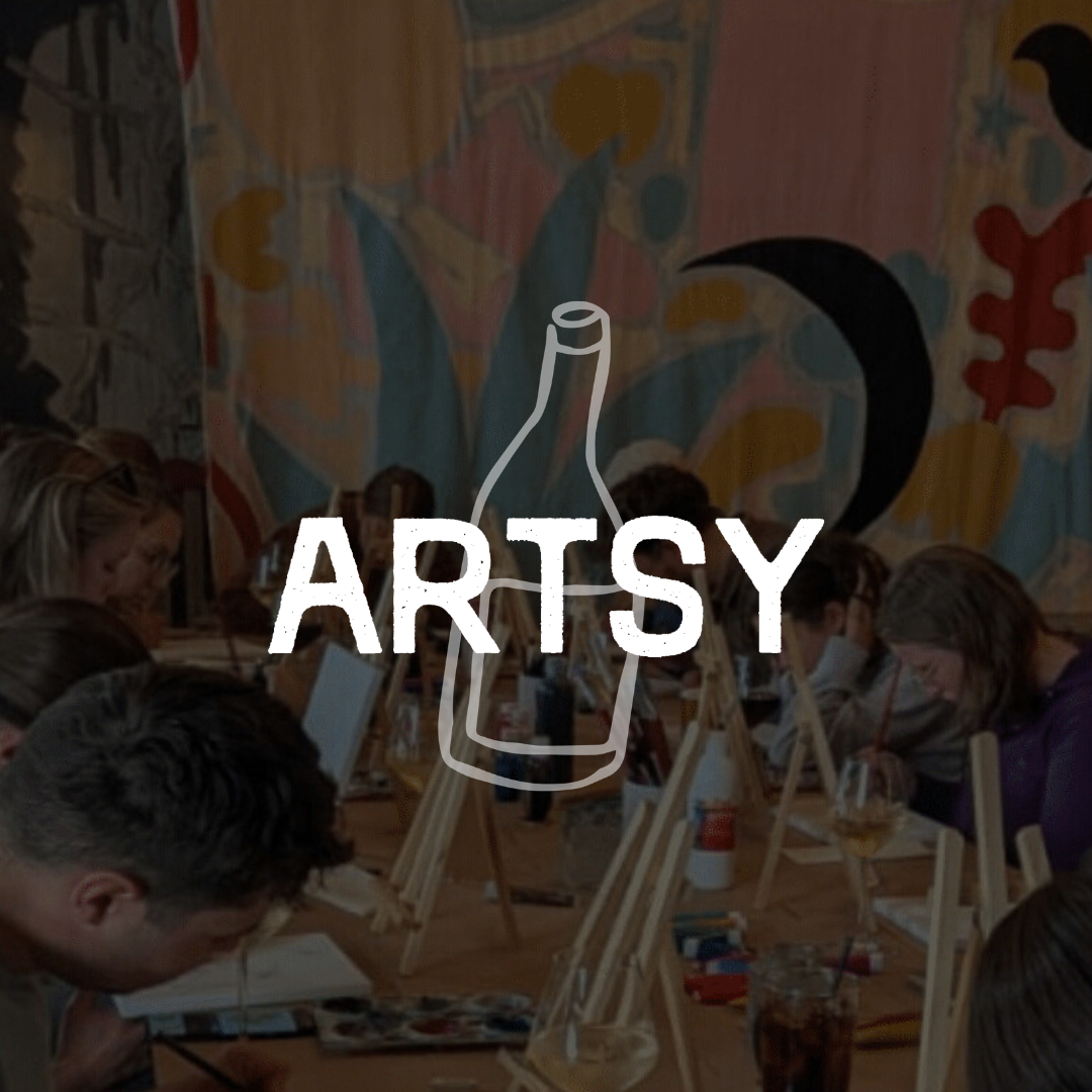Group of people painting on canvases at a long table in a colorful studio.