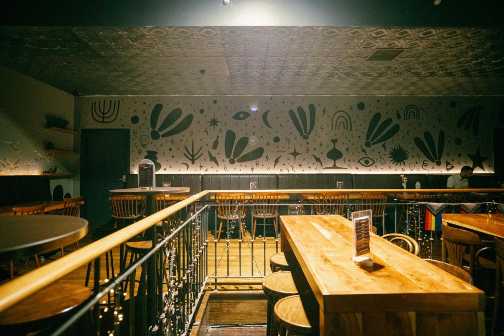 Dimly lit bar interior with a long wooden counter, stools, and a mural of abstract shapes on the back wall