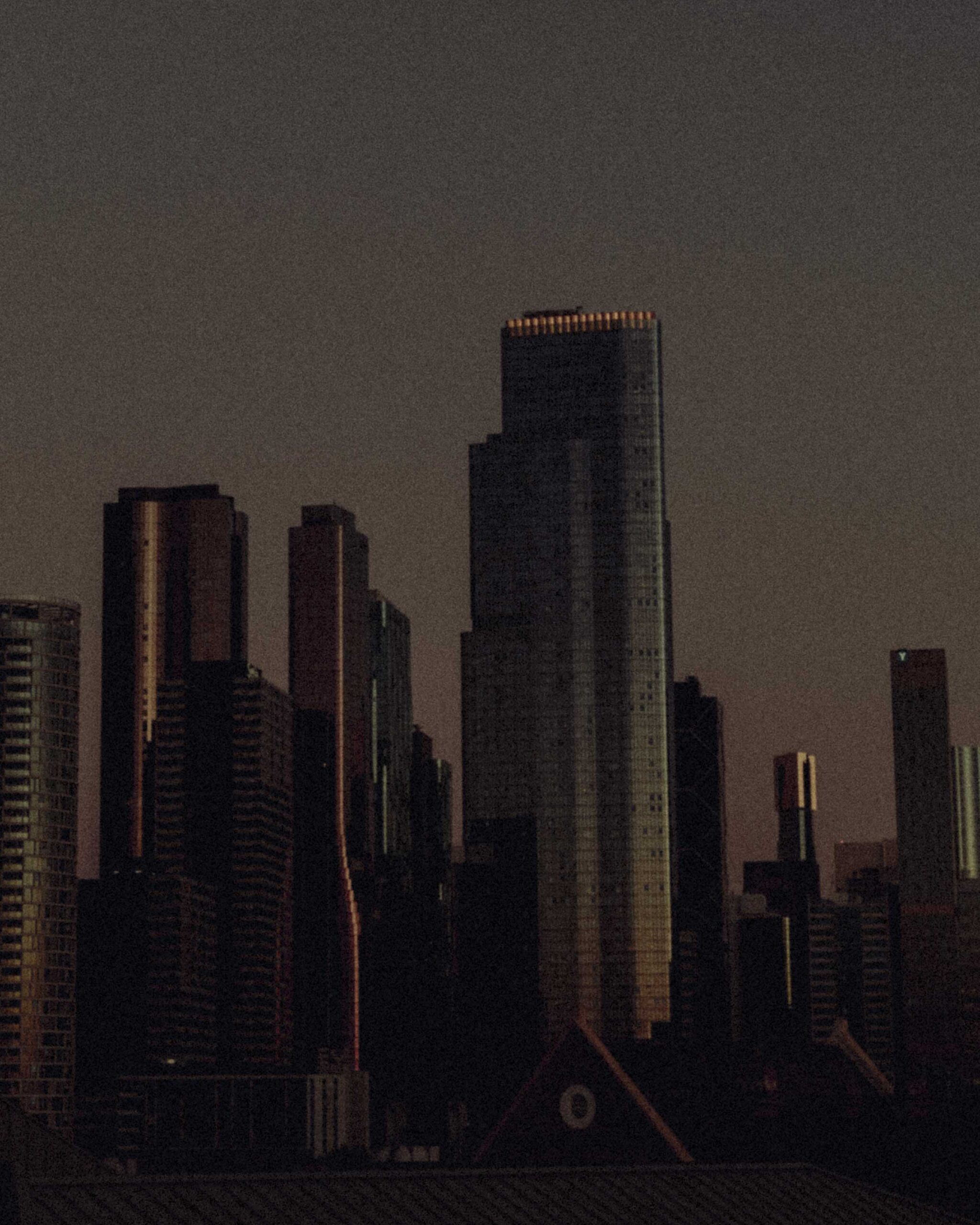 Nighttime city skyline with tall dark skyscrapers; a central tower has orange lights along its top.