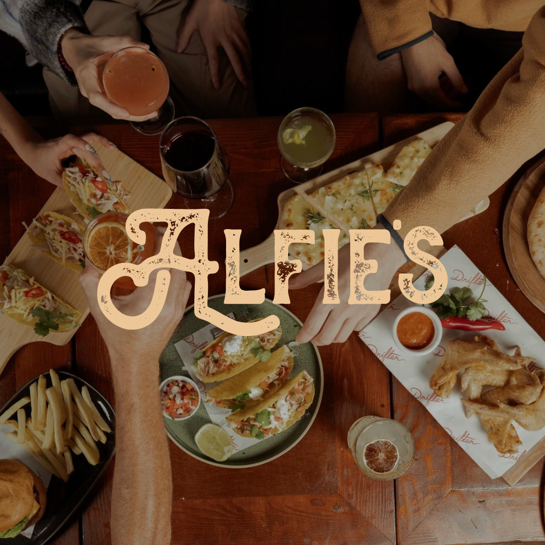 Top-down view of a social dinner with tacos, fries, and drinks on a wooden table; large 'ALFIE'S' branding across the image.