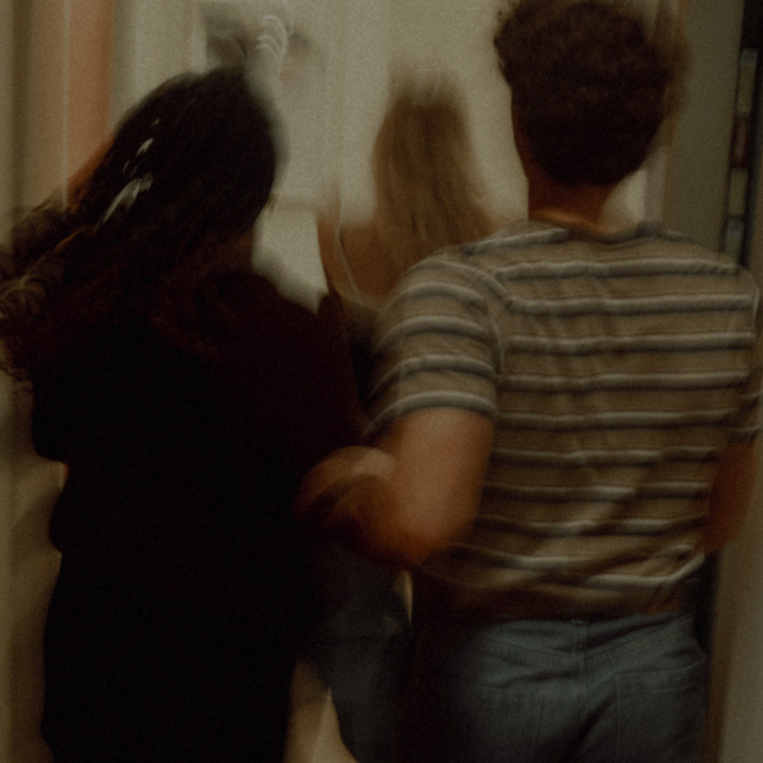 Two adults seen from behind, walking down a dim hallway with motion blur.