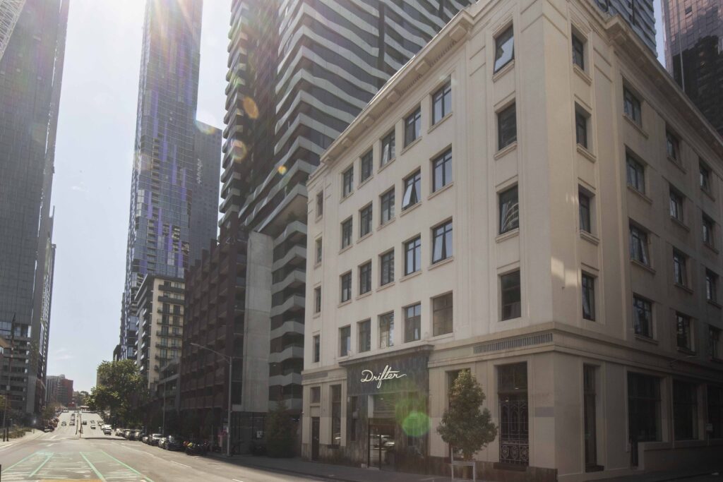 City street with tall glass skyscrapers and a beige corner building with a storefront labeled 'Drifter' on the right.