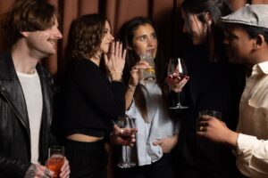Group of friends at a party, holding drinks and chatting together in a dimly lit room.
