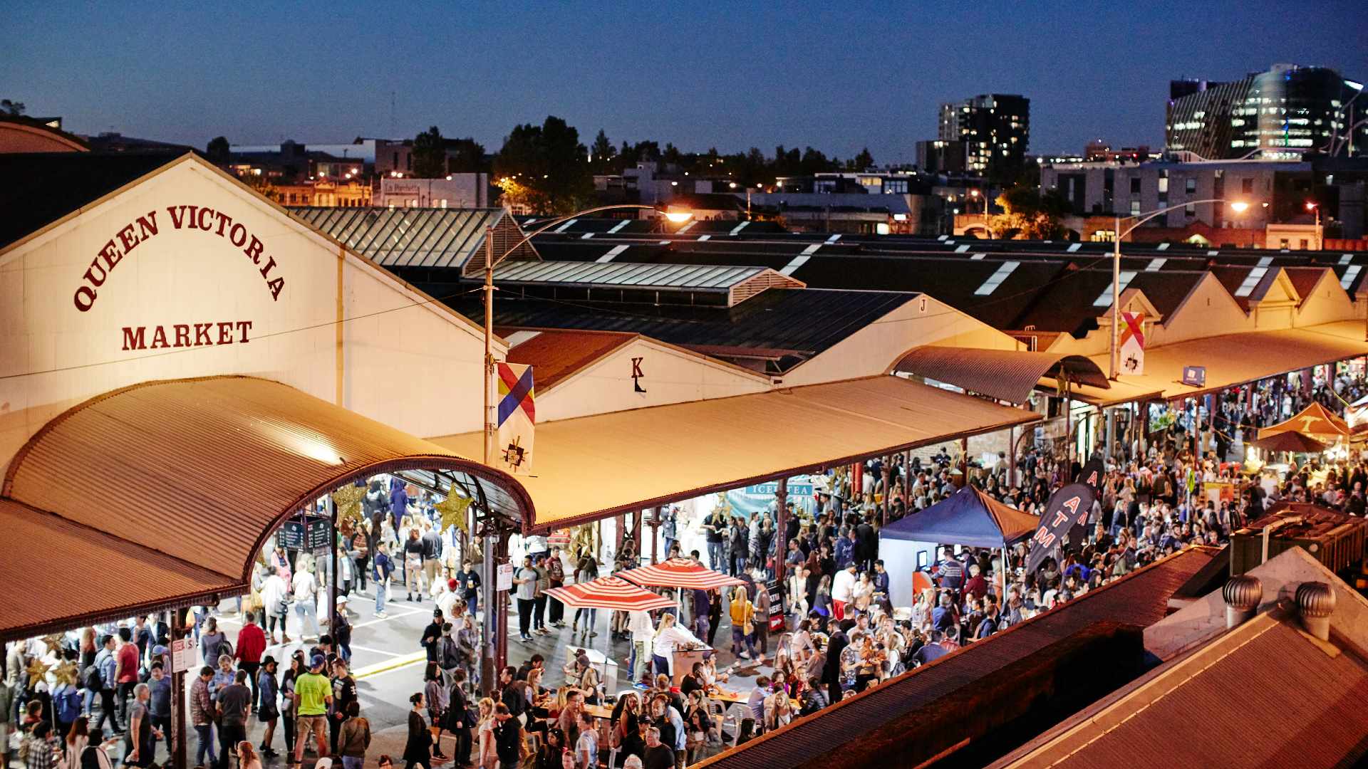 Night view of Queen Victoria Market bustling with people and warm market lights above the stalls at dusk.