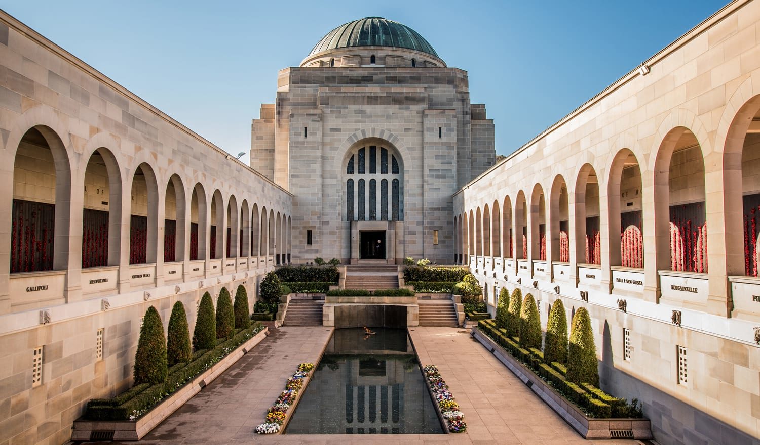 Stone building with a large green-domed central pavilion, flanked by arched colonnades and a rectangular reflecting pool.