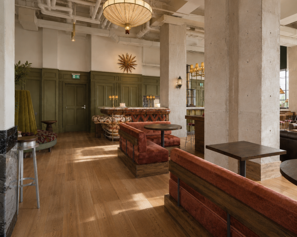 Cozy lounge bar with red velvet banquettes, round tables, and green paneled walls under warm lighting at a stylish venue
