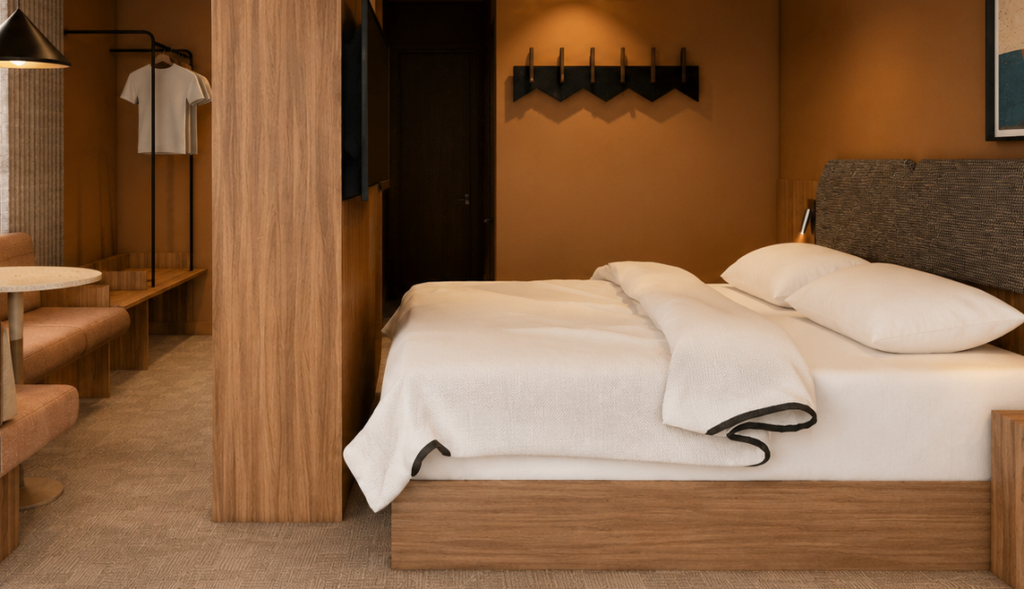 Hotel room with a large bed in white linens, wooden headboard and partition, and a seating area to the left with a coat rack on the wall behind.