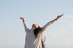 Person with arms raised toward the sky, celebrating outdoors against a clear blue backdrop.
