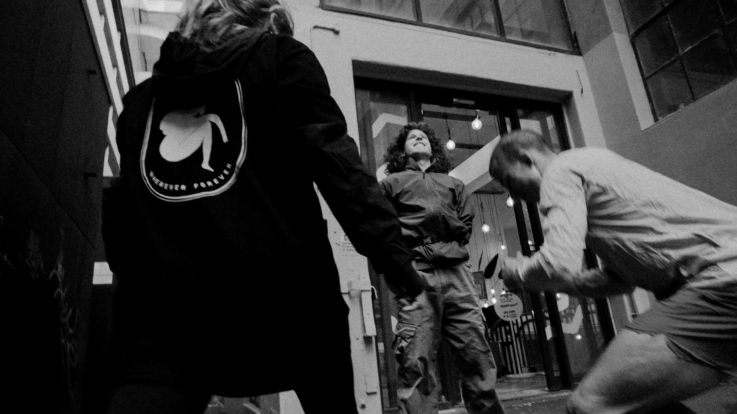 Black-and-white photo of four people standing in a doorway, arms linked in a circle, one person smiling at the center.