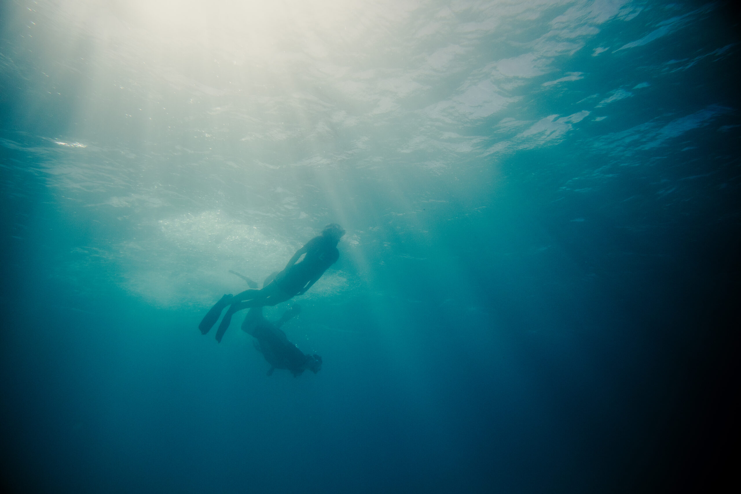 Two scuba divers swimming underwater as sunlight beams through the blue water.