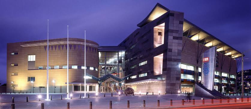 Modern multi-wing building lit at dusk, featuring a glass entrance and flagpoles in front.