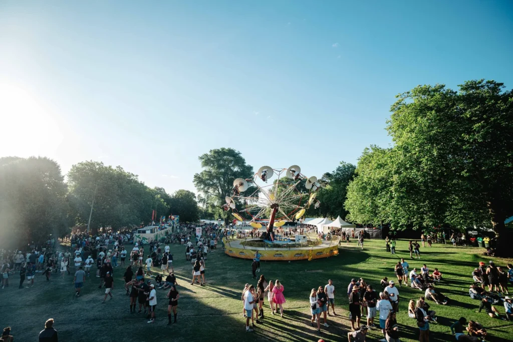 Crowd enjoying a sunny park festival around a circular Ferris wheel ride with tents in the background.